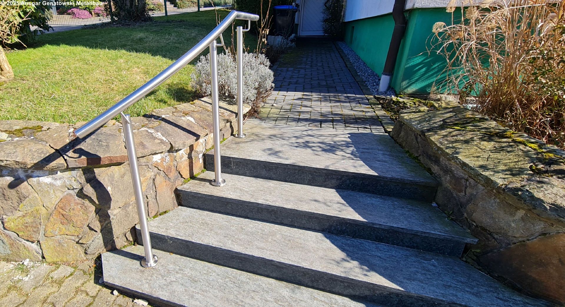 Eine Betontreppe führt zu einem Türrahmen mit einem Handlauf aus Edelstahl auf der linken Seite.