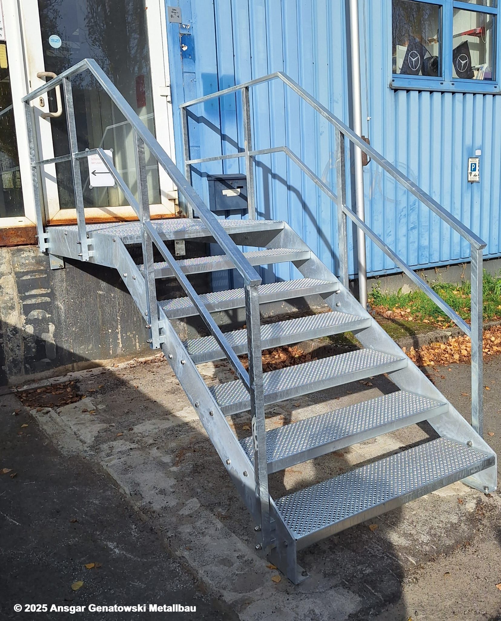 Eine metallene Außentreppe mit Handlauf führt zu einem hellblauen Gebäude.