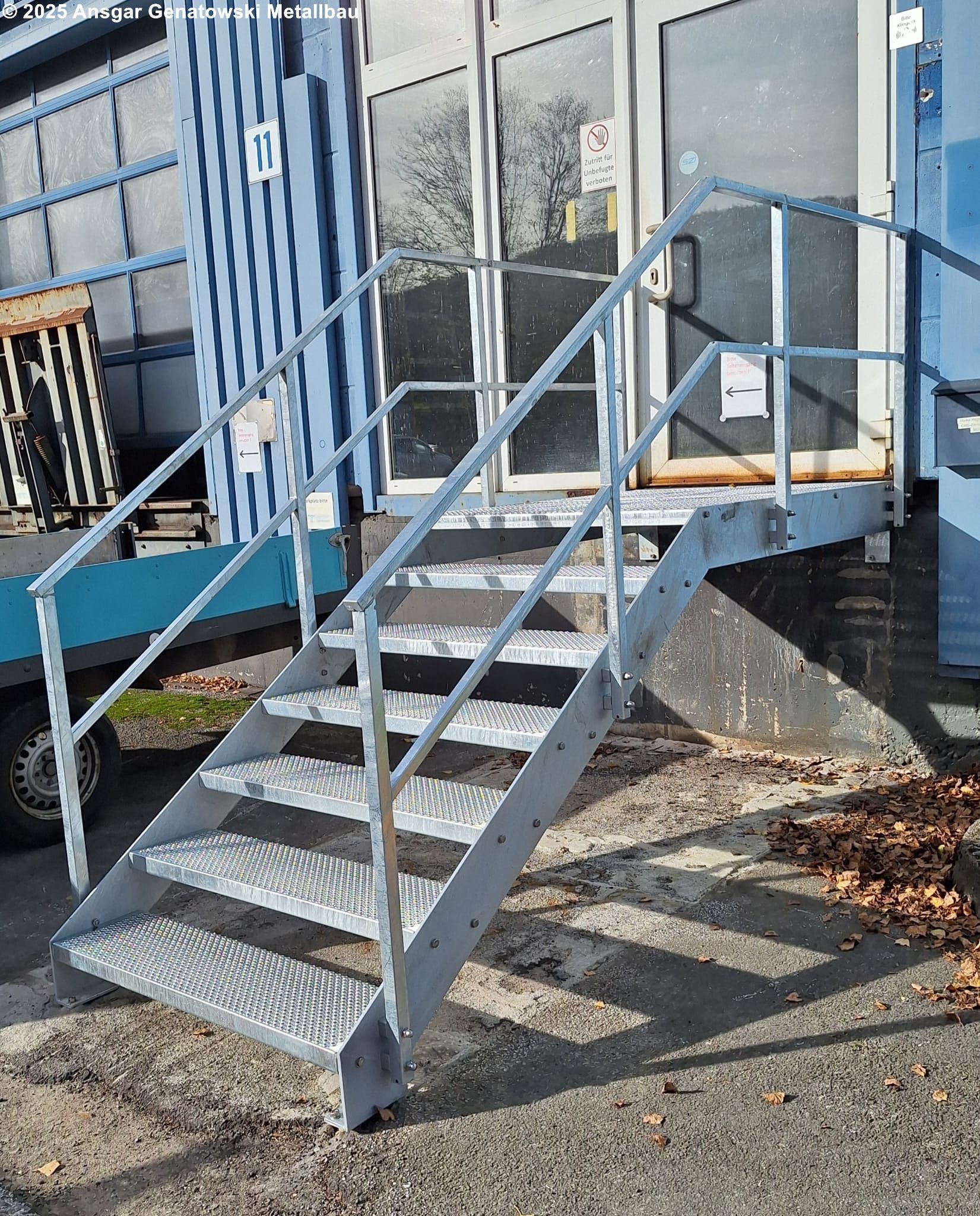 Metalltreppe, die zu einer Tür führt. Graues Metallgeländer und Stufen. Gebäude im Hintergrund.