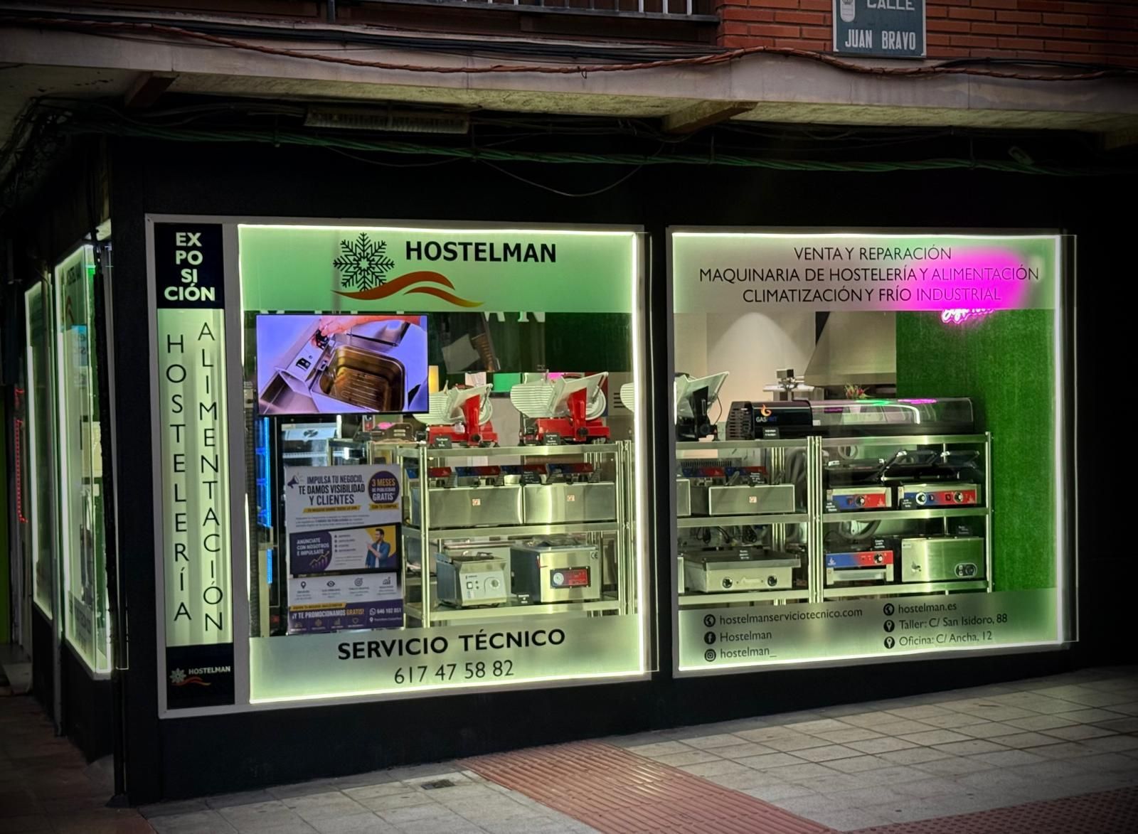 Fachada iluminada por la noche con escaparates verdes para un taller de servicio técnico.