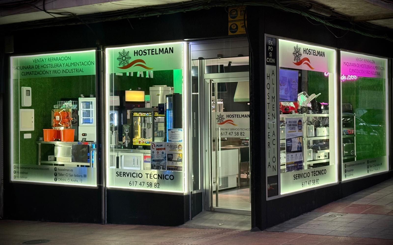 Esquina de una tienda con escaparates iluminados de color verde brillante y rosa por la noche.