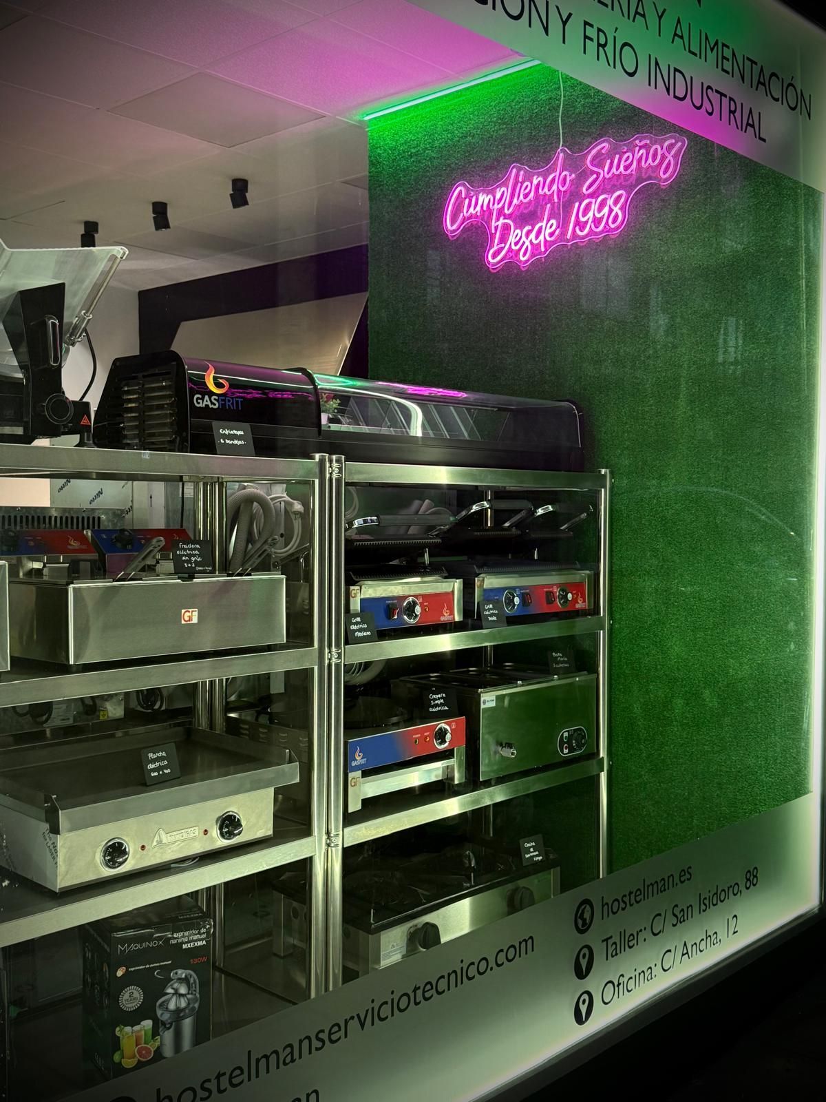 Cabina de DJ de estilo retro con estantes para equipos, letrero de neón rosa y pared iluminada en verde en un espacio interior con poca luz.