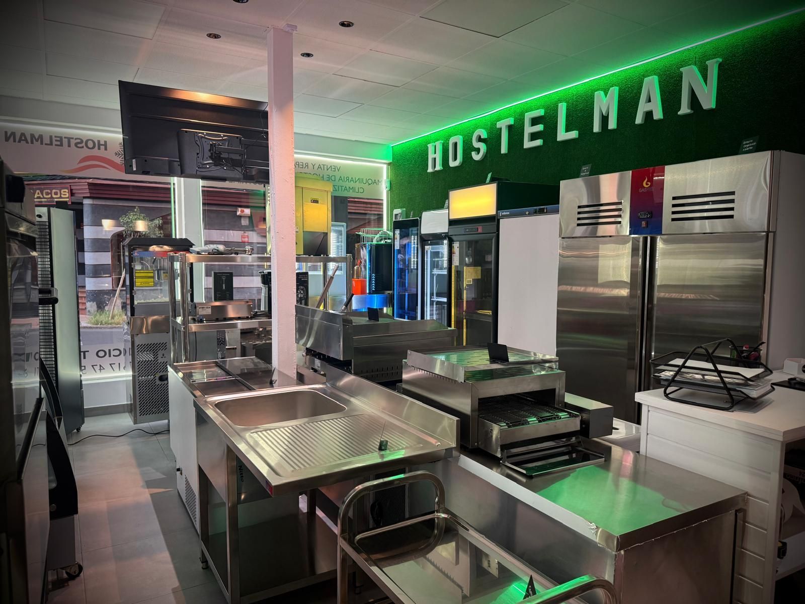 Cafetería moderna vacía con mostradores de acero inoxidable y letrero verde de HOSTELMAN.