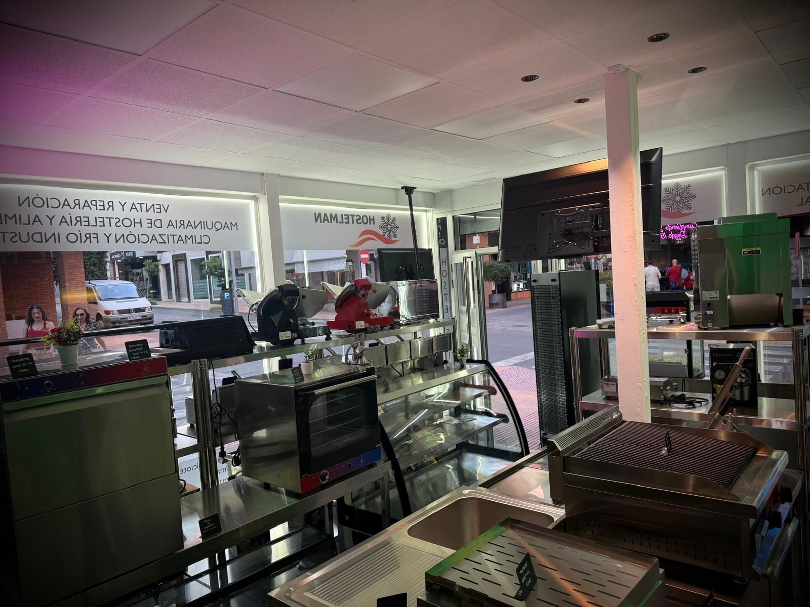 Interior de una pequeña tienda o cafetería con vitrinas, mostradores, estantes e iluminación rosada.