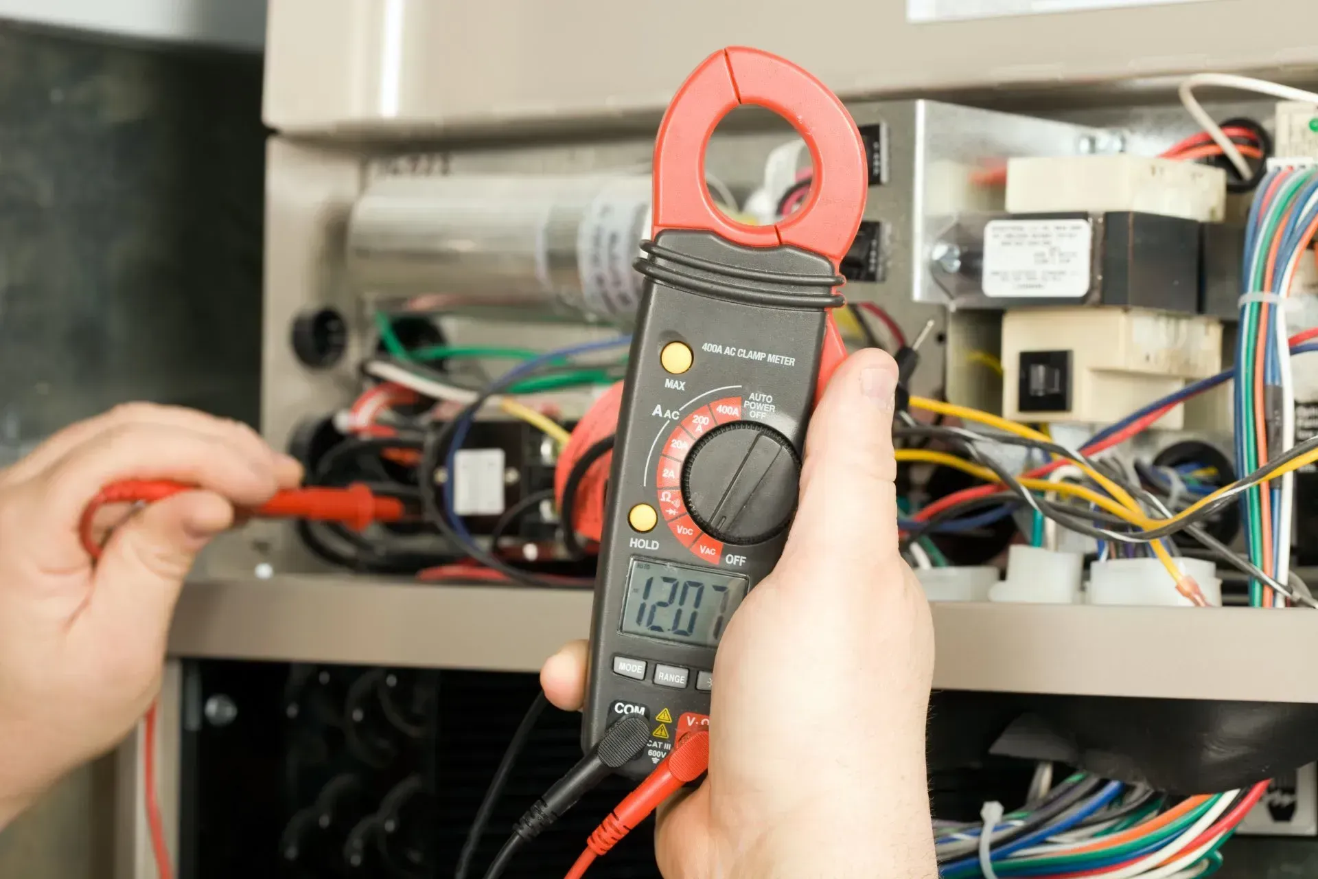 Des mains utilisent une pince ampèremétrique pour tester le câblage à l'intérieur d'un panneau électrique ouvert.