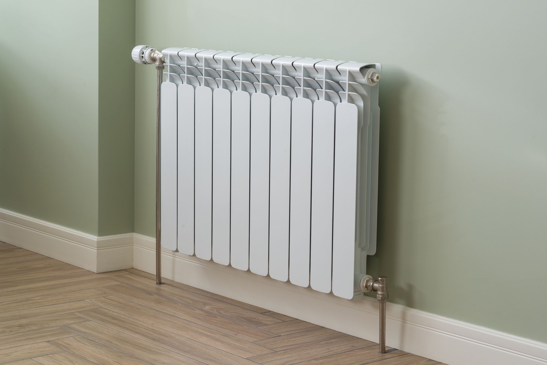 Radiateur blanc sur un mur vert pâle, avec parquet et plinthes blanches.