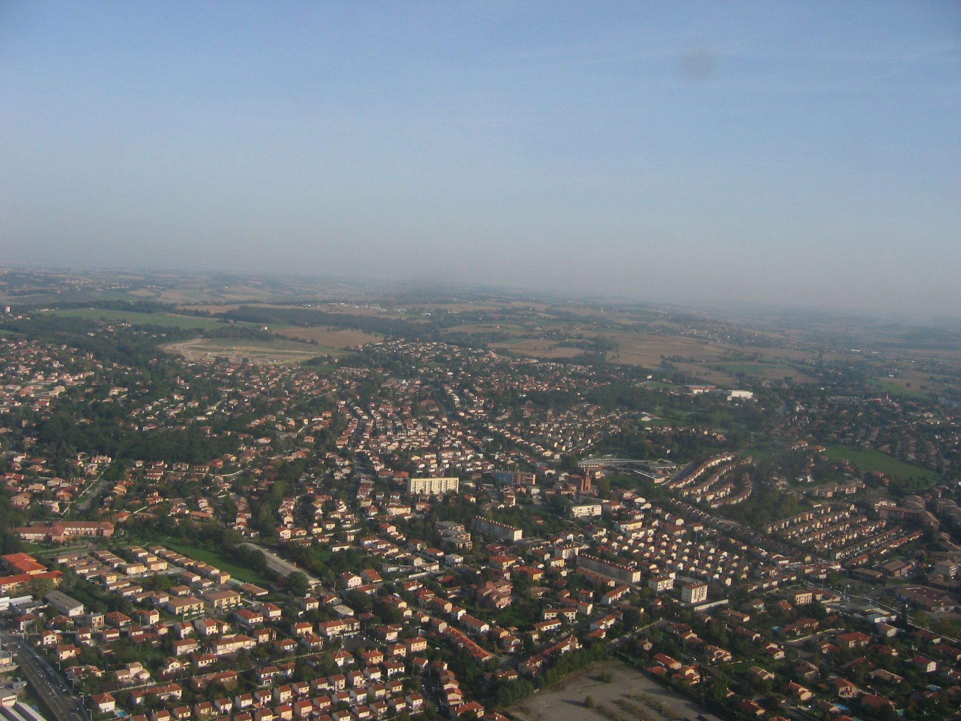 Vue aérienne d'un vaste quartier de banlieue avec des maisons aux toits rouges sous un ciel brumeux