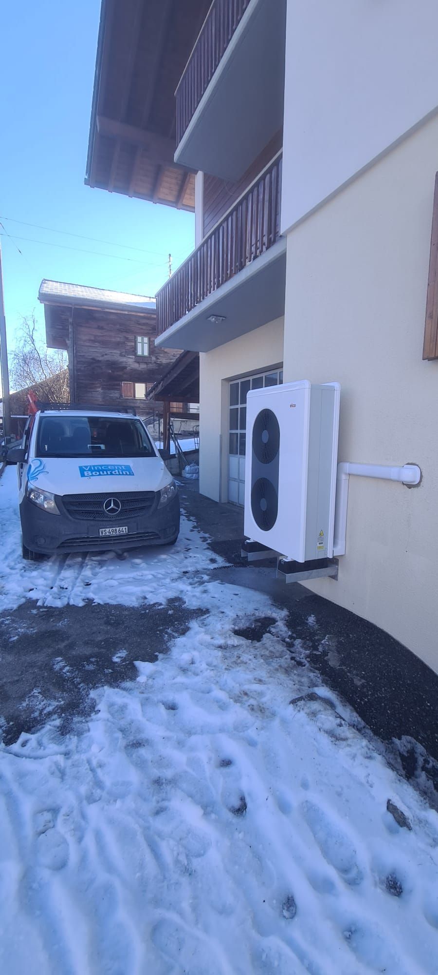 Une camionnette blanche est garée devant un bâtiment sous la neige | Vincent Bourdin Sàrl