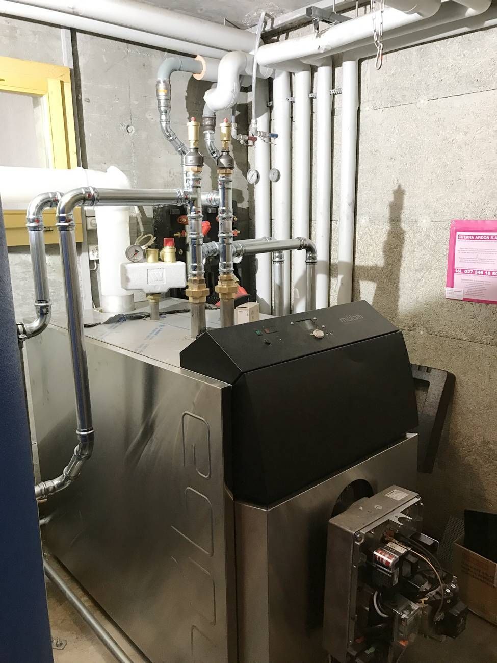 Une grande chaudière en acier inoxydable se trouve dans une pièce avec des tuyaux | Vincent Bourdin Sàrl