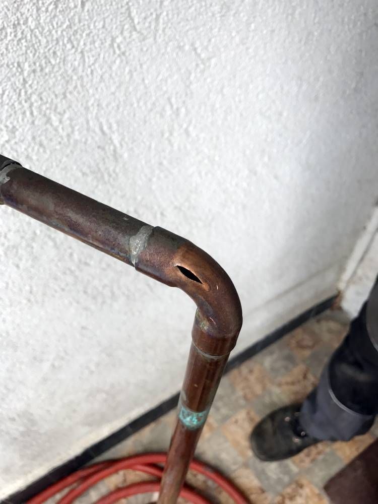 Une personne se tient à côté d'un tuyau en cuivre avec un trou dedans | Vincent Bourdin Sàrl