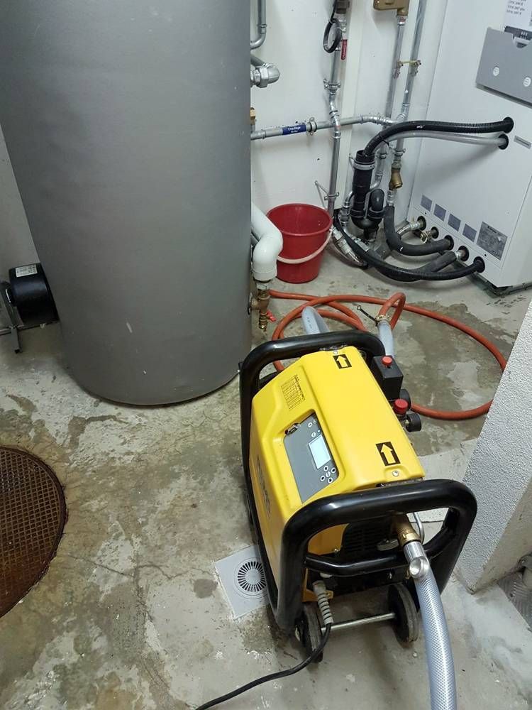 Une machine jaune est assise dans une pièce à côté d'un chauffe-eau | Vincent Bourdin Sàrl