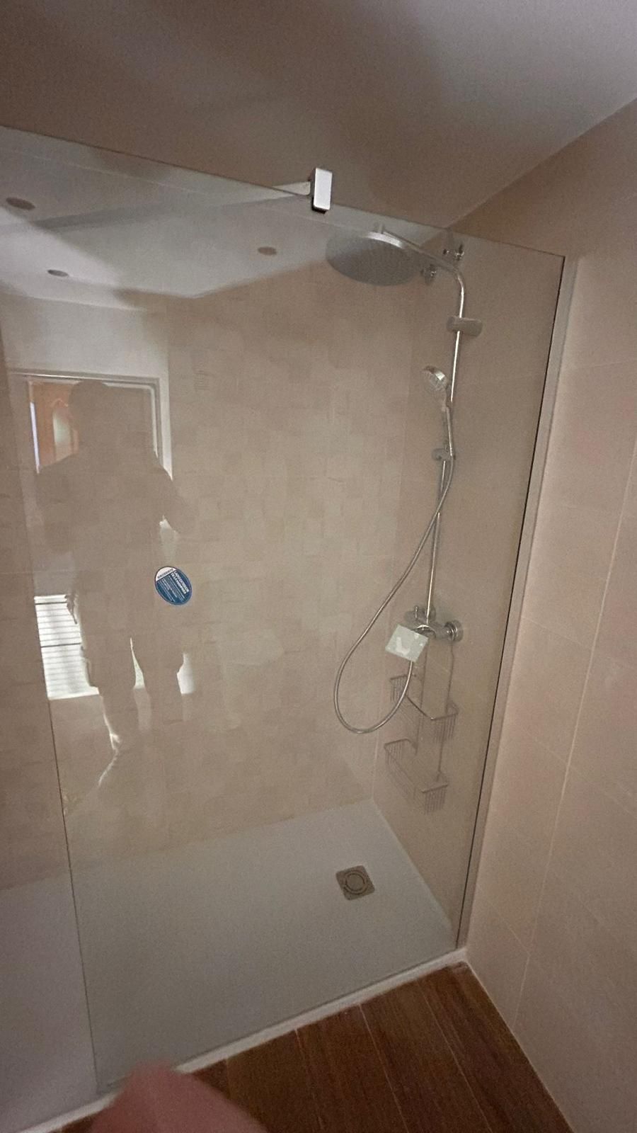 Cabina de ducha con puerta de cristal, cabezal de ducha tipo lluvia, ducha de mano y paredes de color beige.