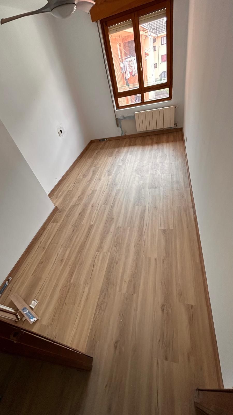 Una habitación vacía con suelo de madera, una ventana y paredes blancas.