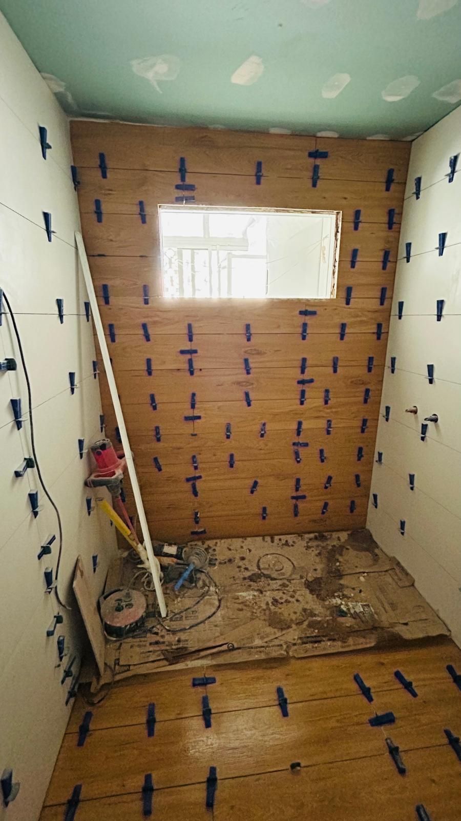 Remodelación de baño en progreso: paredes de madera, clips niveladores de azulejos azules, ventana, herramientas.