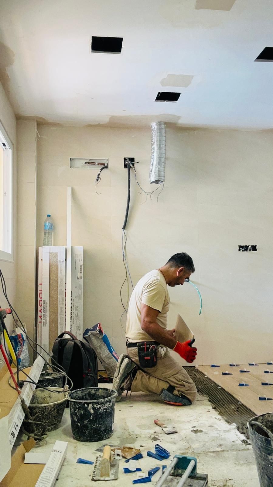 Persona arrodillada, trabajando en la instalación de baldosas en el piso de una habitación en construcción.