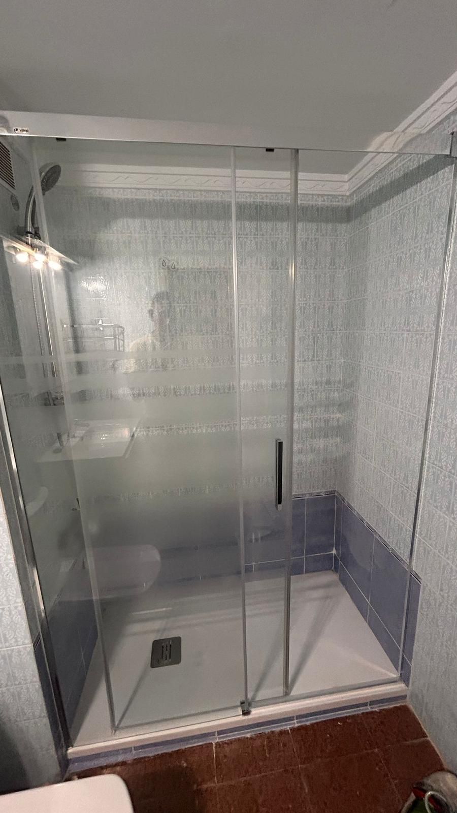 Cabina de ducha de cristal con puerta corredera, azulejos azules y plato de ducha blanco.