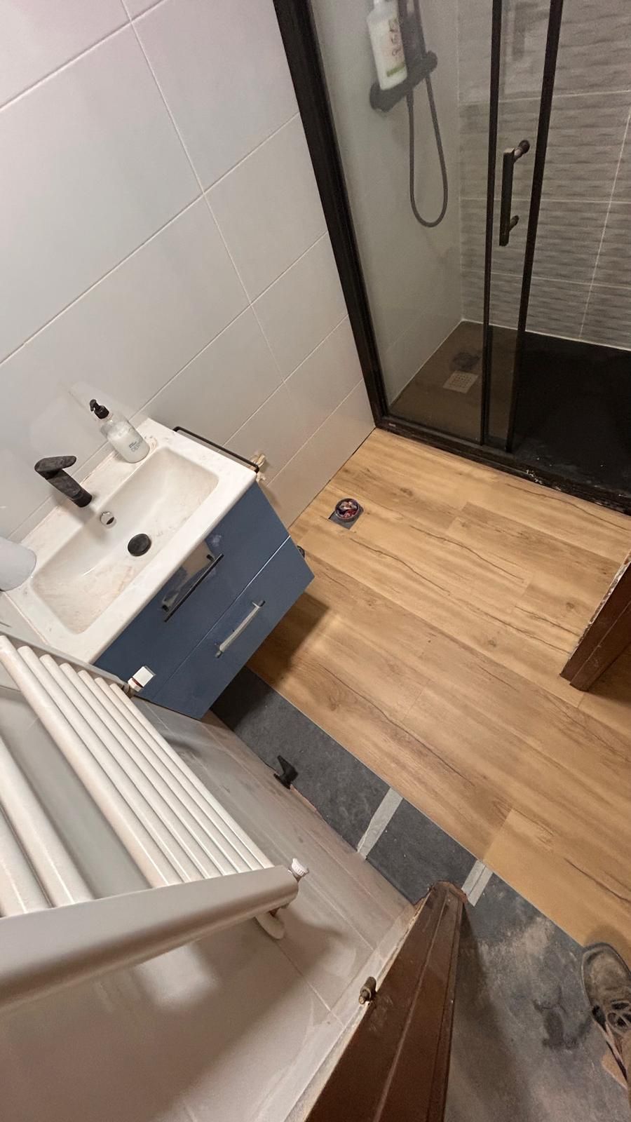 Baño con lavabo azul, ducha con marco negro y suelo imitación madera.