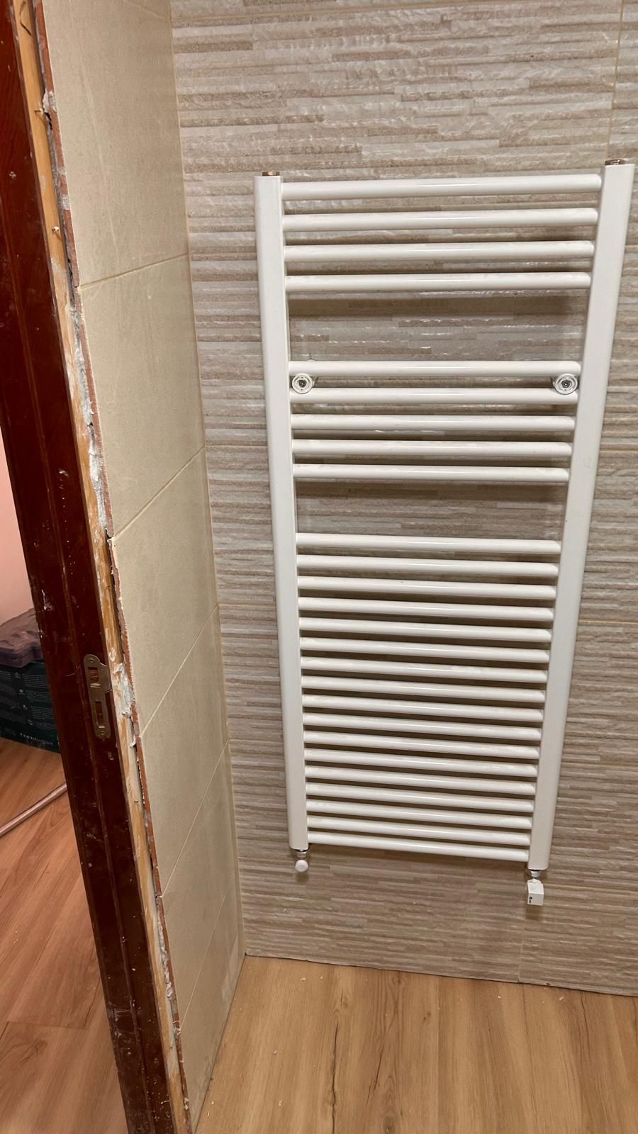 Calentador de toallas blanco montado en una pared de baño alicatada.