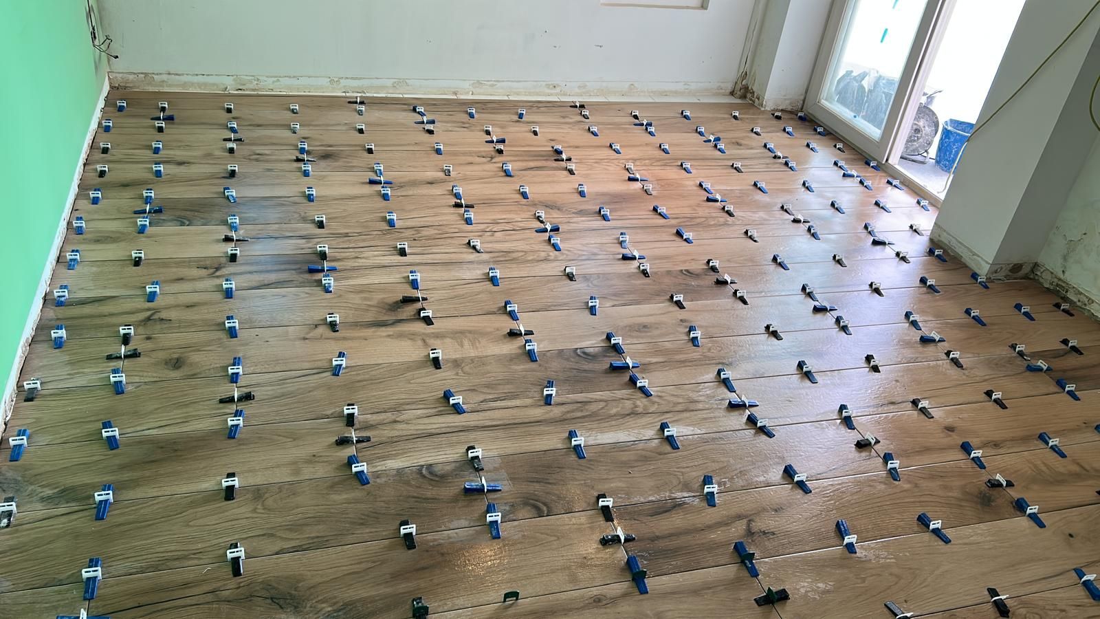 Habitación con piso marrón, espaciadores azules instalados en todas partes y pared verde.