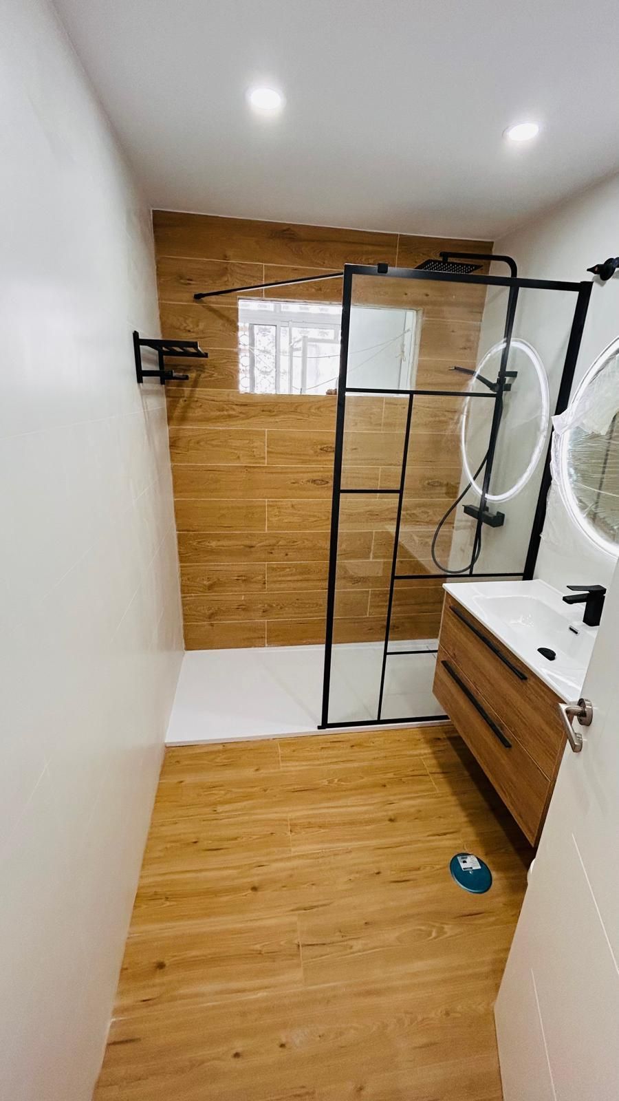 Baño moderno: pisos y azulejos de pared con apariencia de madera, ducha con marco negro y puerta de vidrio