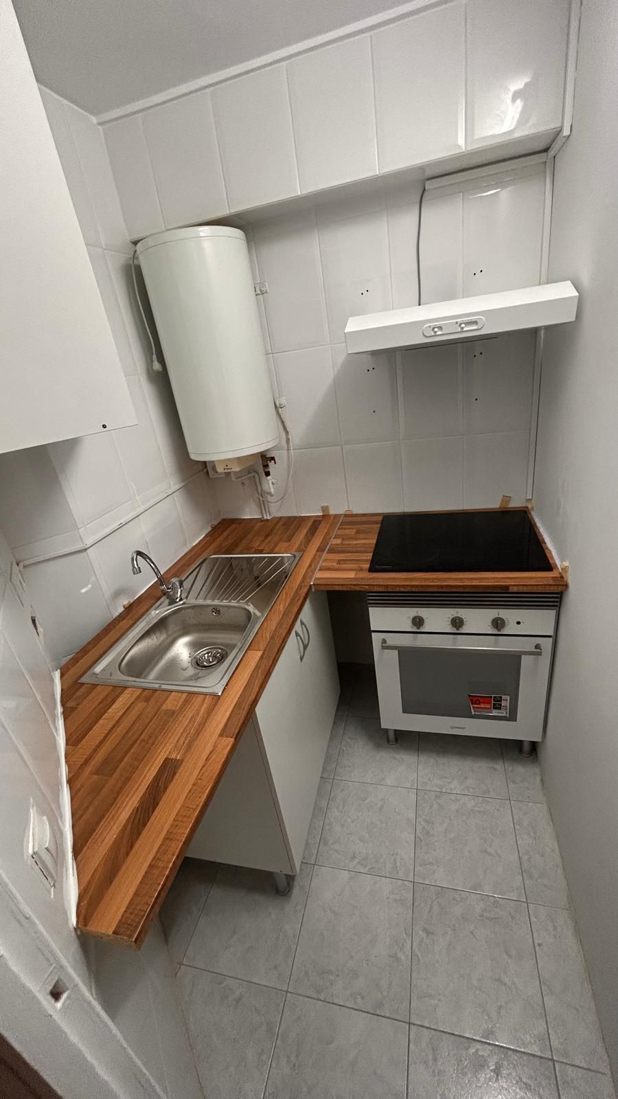 Pequeña cocina con encimeras de madera, gabinetes blancos y estufa.