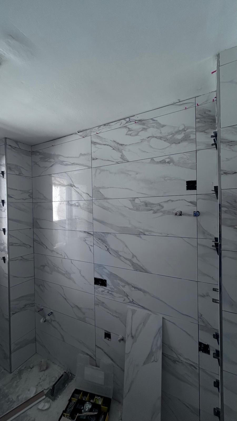 Baño con paredes parcialmente alicatadas, baldosas tipo mármol blanco con vetas grises, espaciadores visibles