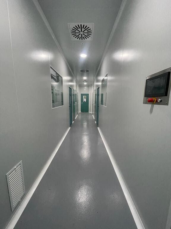Un largo pasillo en un hospital con paredes blancas y una puerta verde.