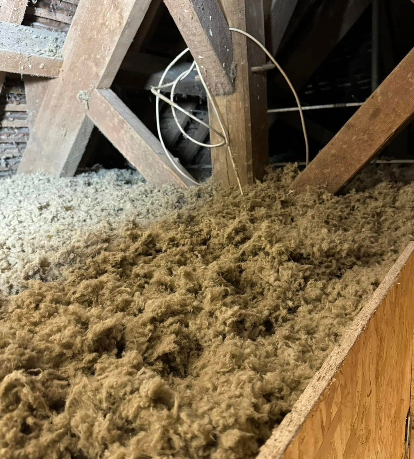 Intérieur du grenier avec isolation fibreuse brune entre les poutres et les planches en bois.