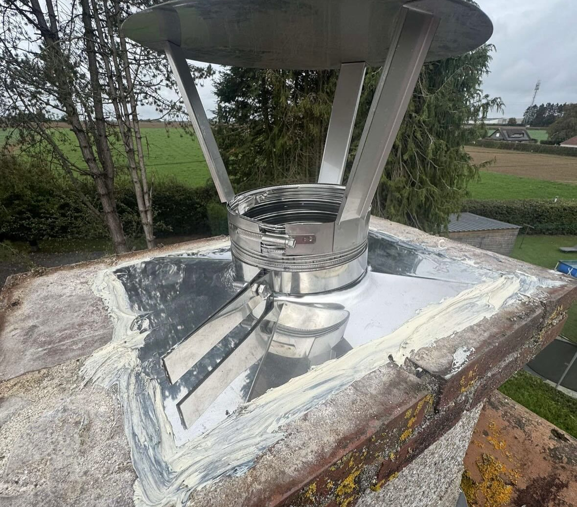 Gros plan sur le sommet d'une cheminée extérieure avec un chapeau en acier inoxydable et une solin métallique.