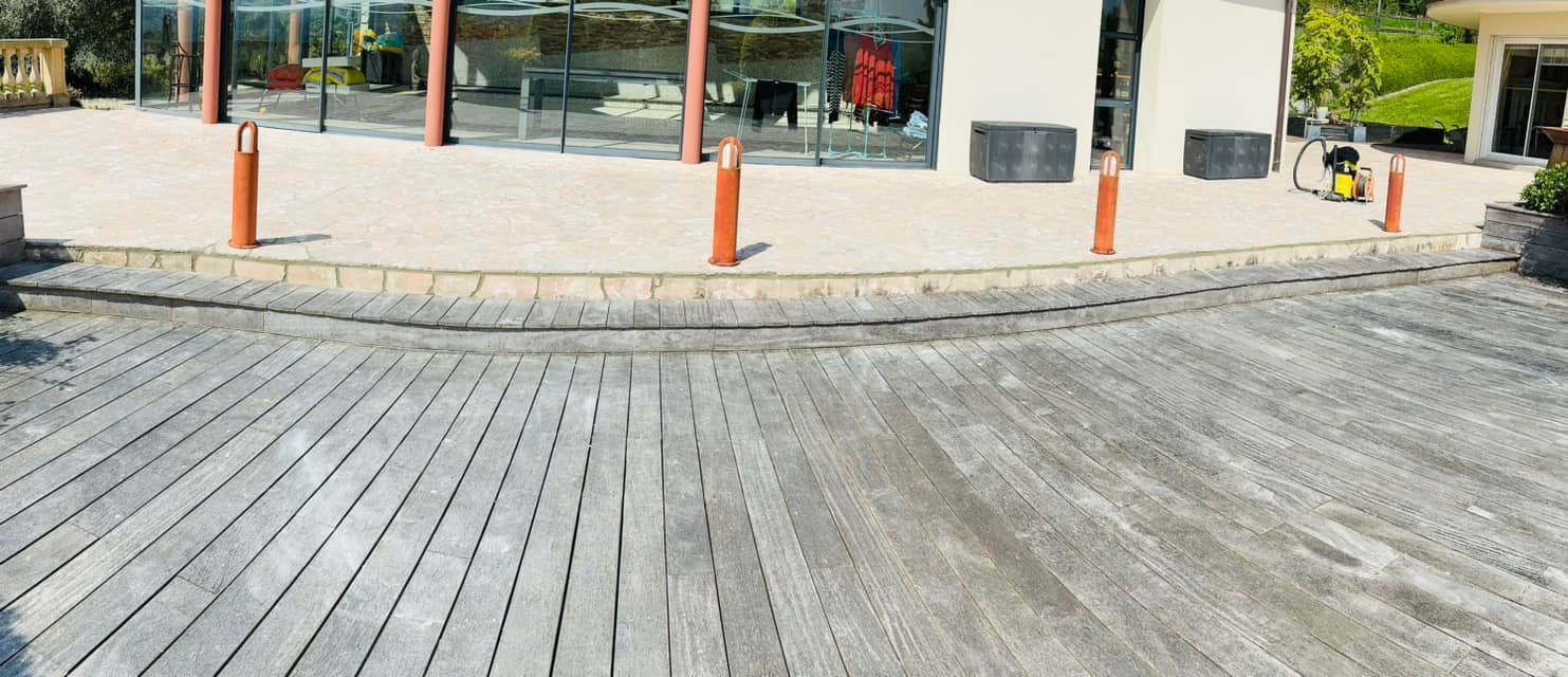 Passerelle en bois menant à un bâtiment aux fenêtres vitrées, bordée de bornes orange.