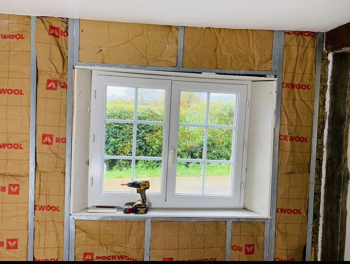 Mur intérieur avec isolation apparente et cadre de fenêtre. Une perceuse est posée sur le rebord de la fenêtre.