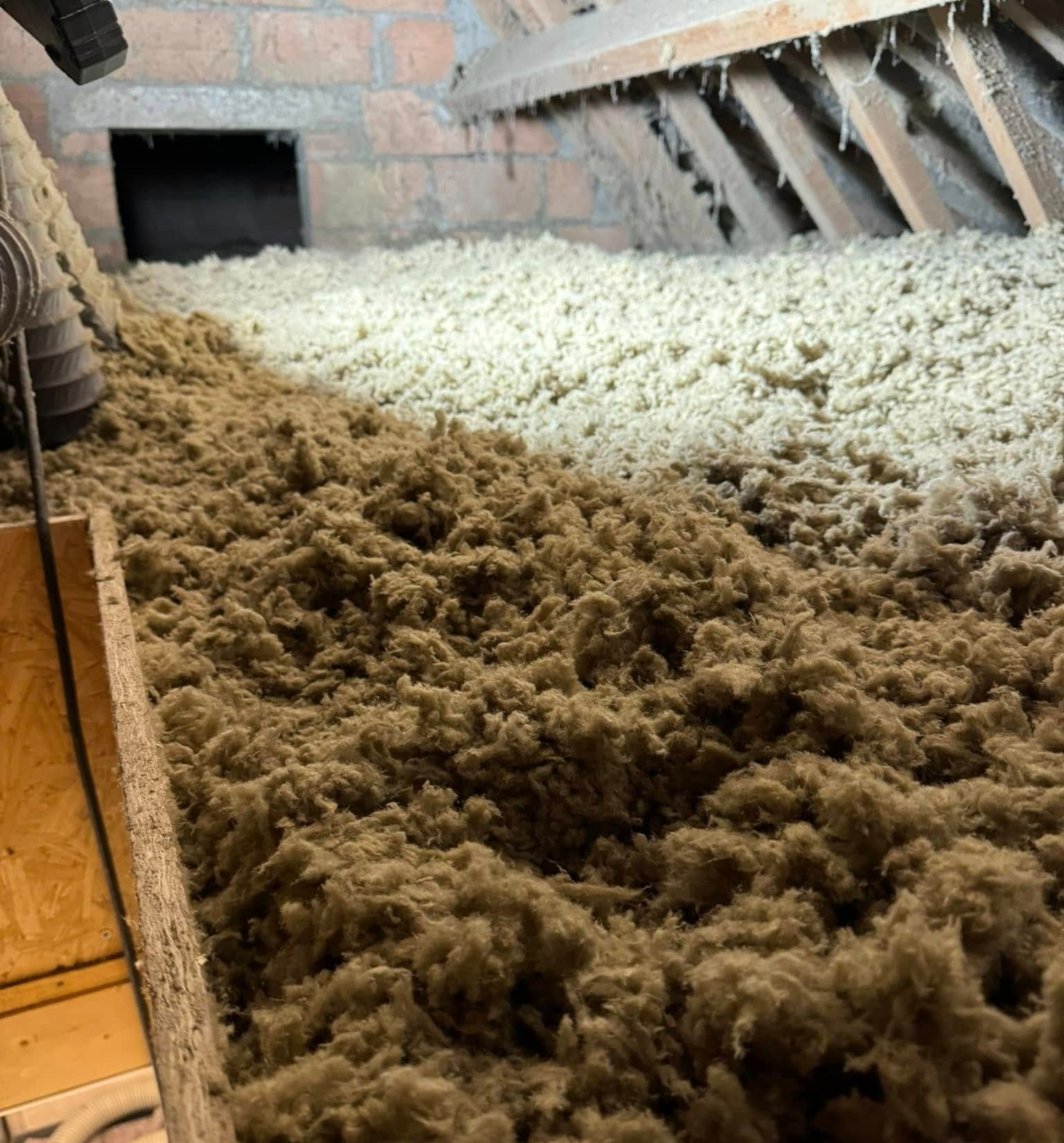 Grenier avec une épaisse isolation brune entassée entre les poutres en bois.