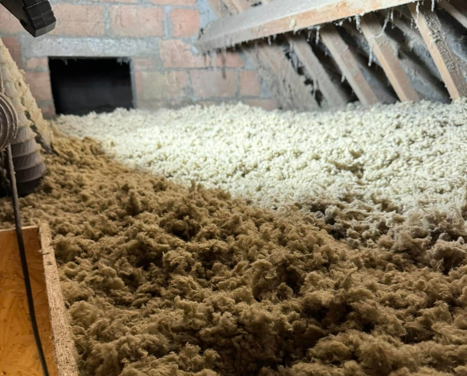 Combles remplis d'isolant brun et blanc, mur de briques apparent.