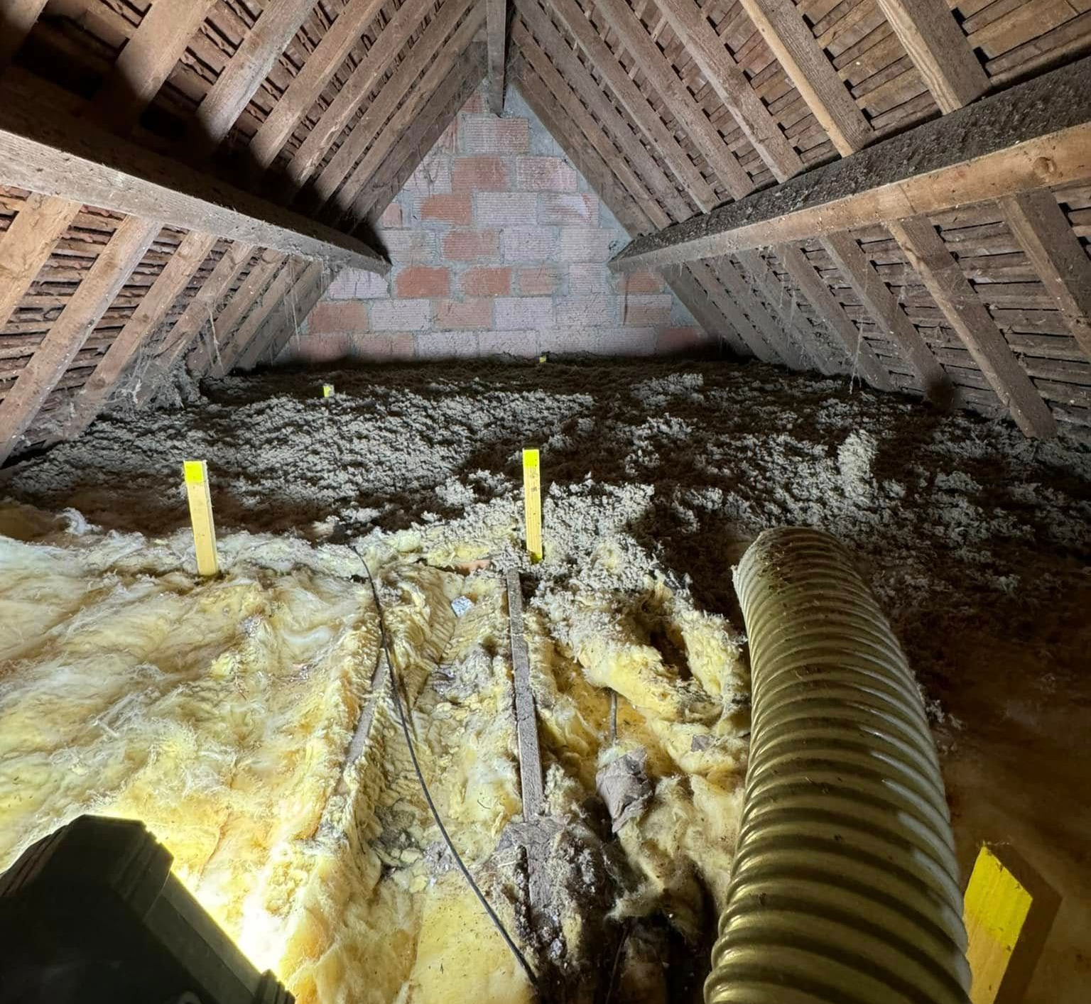 Grenier isolé, poutres en bois, mur en briques et tuyau d'aspirateur, éclairé par une lampe de travail.