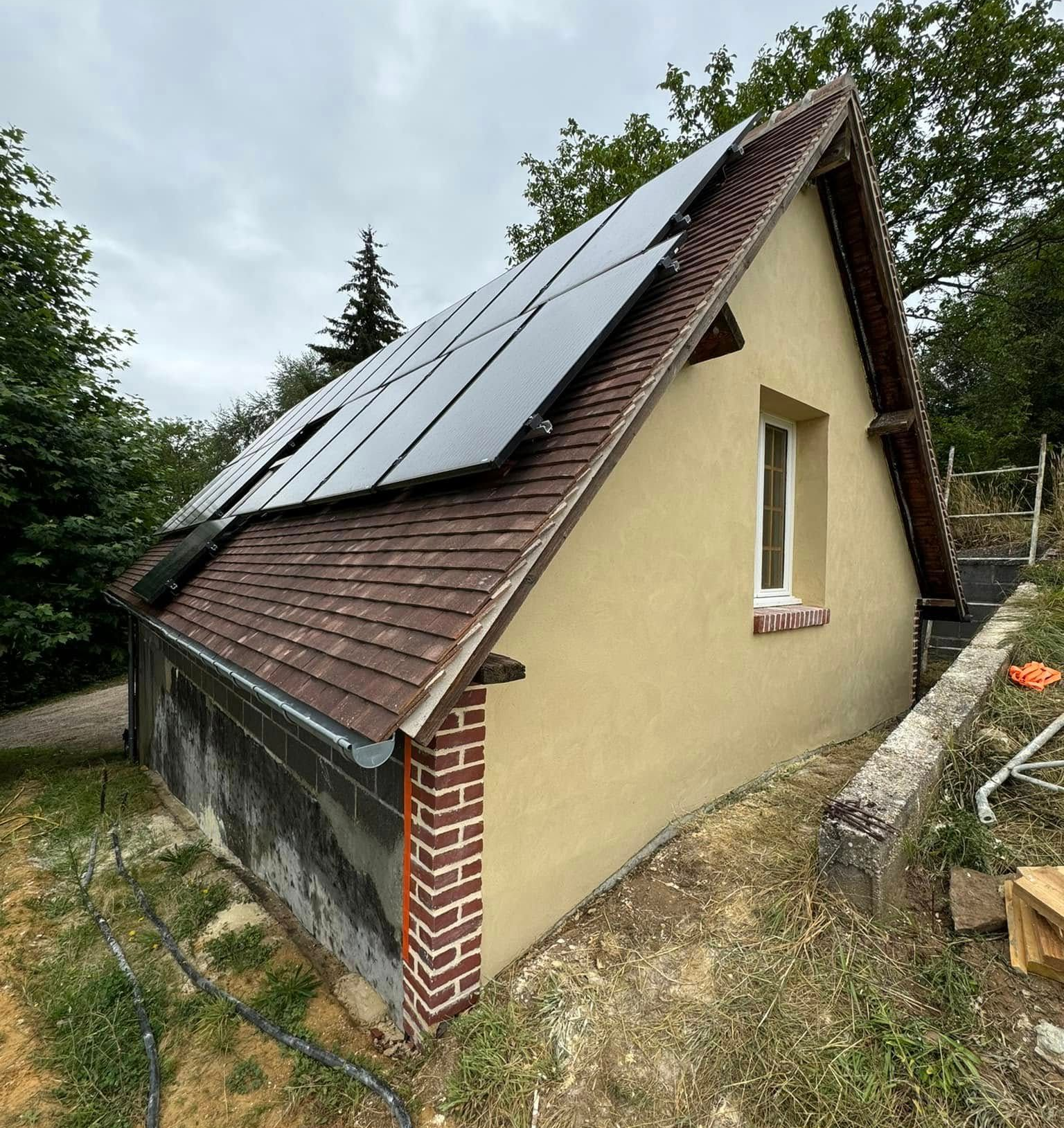 Panneaux solaires sur un bâtiment en briques beiges, avec un toit marron et une petite fenêtre.