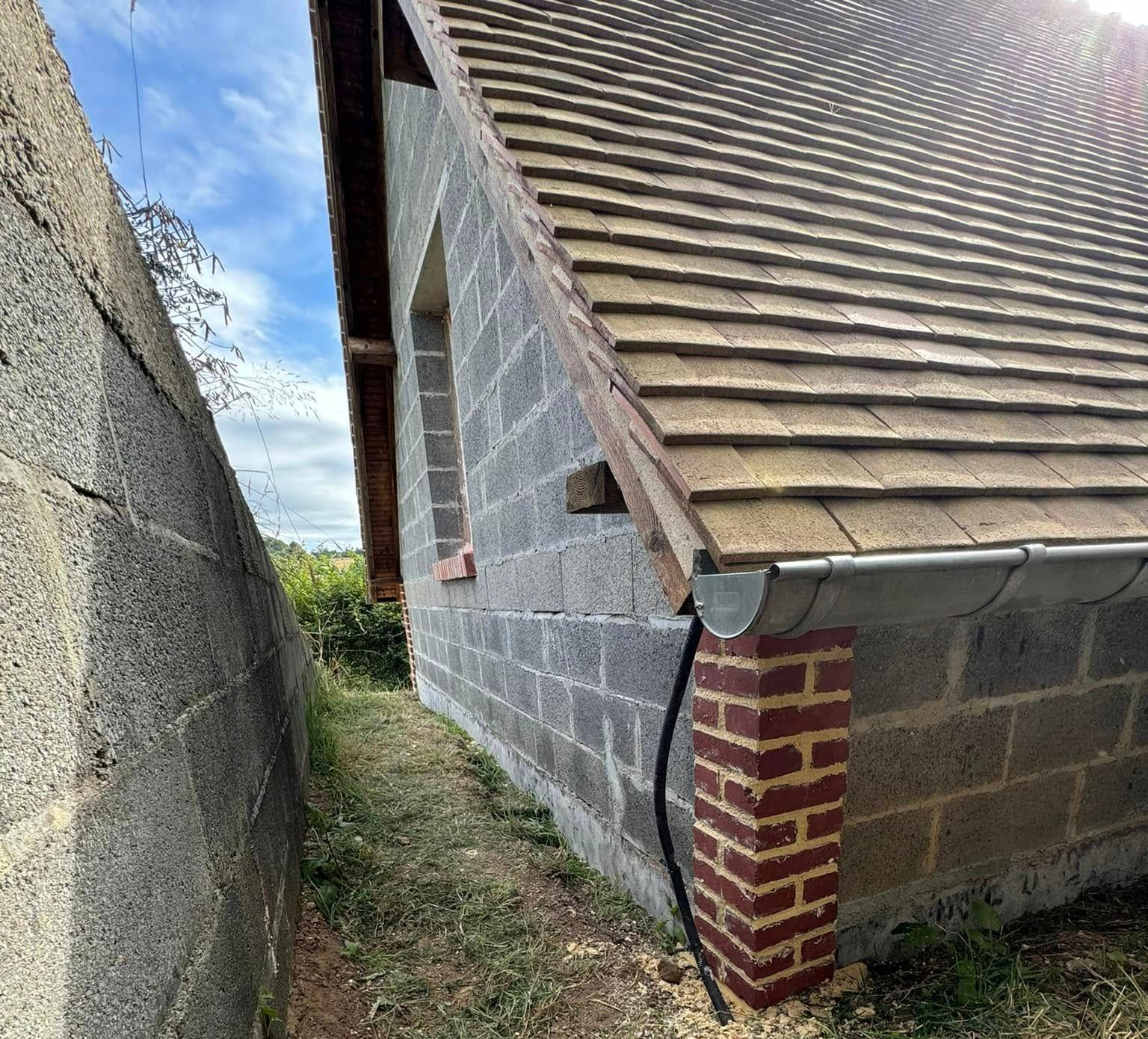 Bâtiment en briques et parpaings avec un toit en pente, adossé à un mur gris.