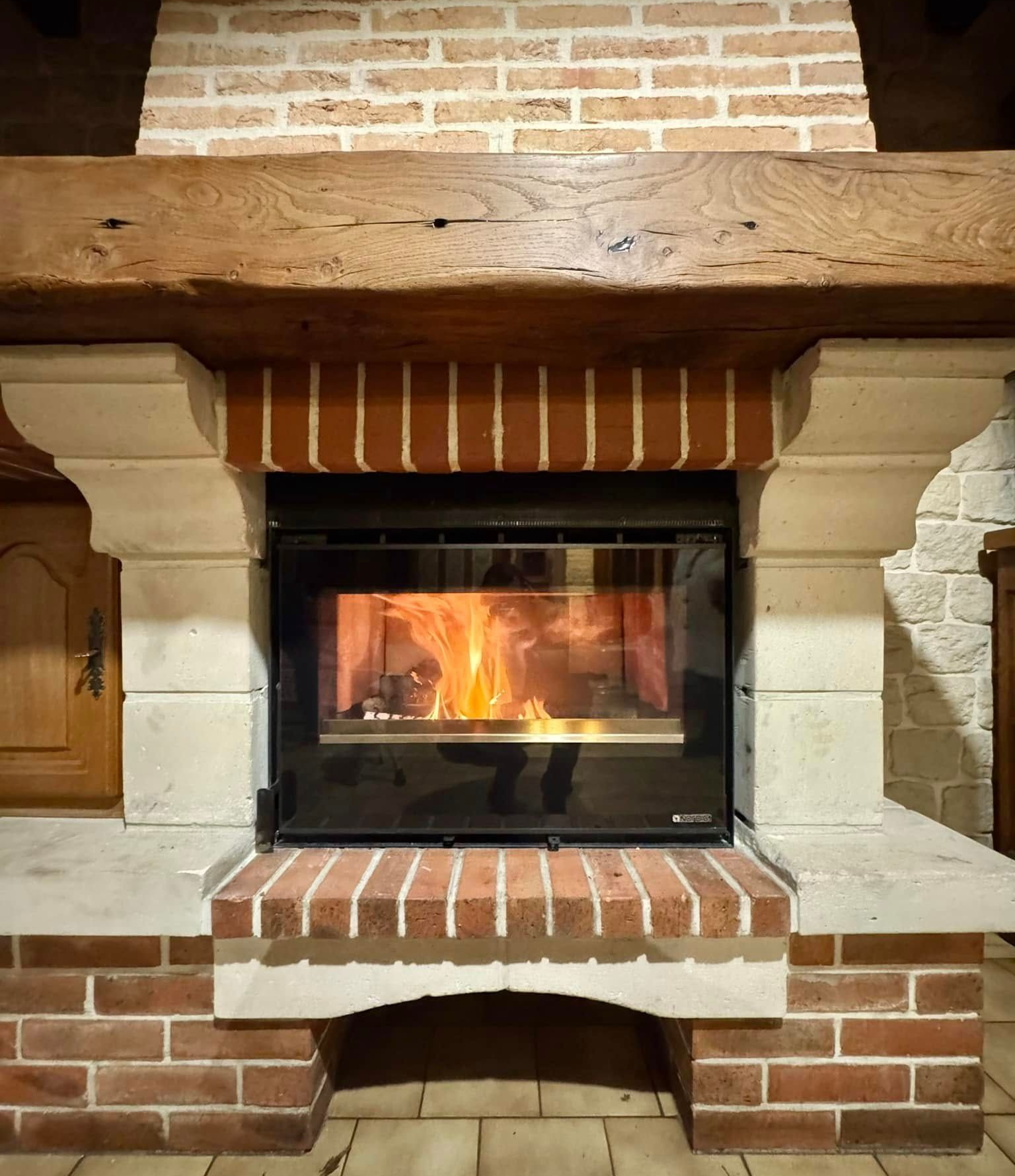 Cheminée avec flammes, maçonnerie de briques, éléments en pierre et manteau de cheminée en poutre de bois.