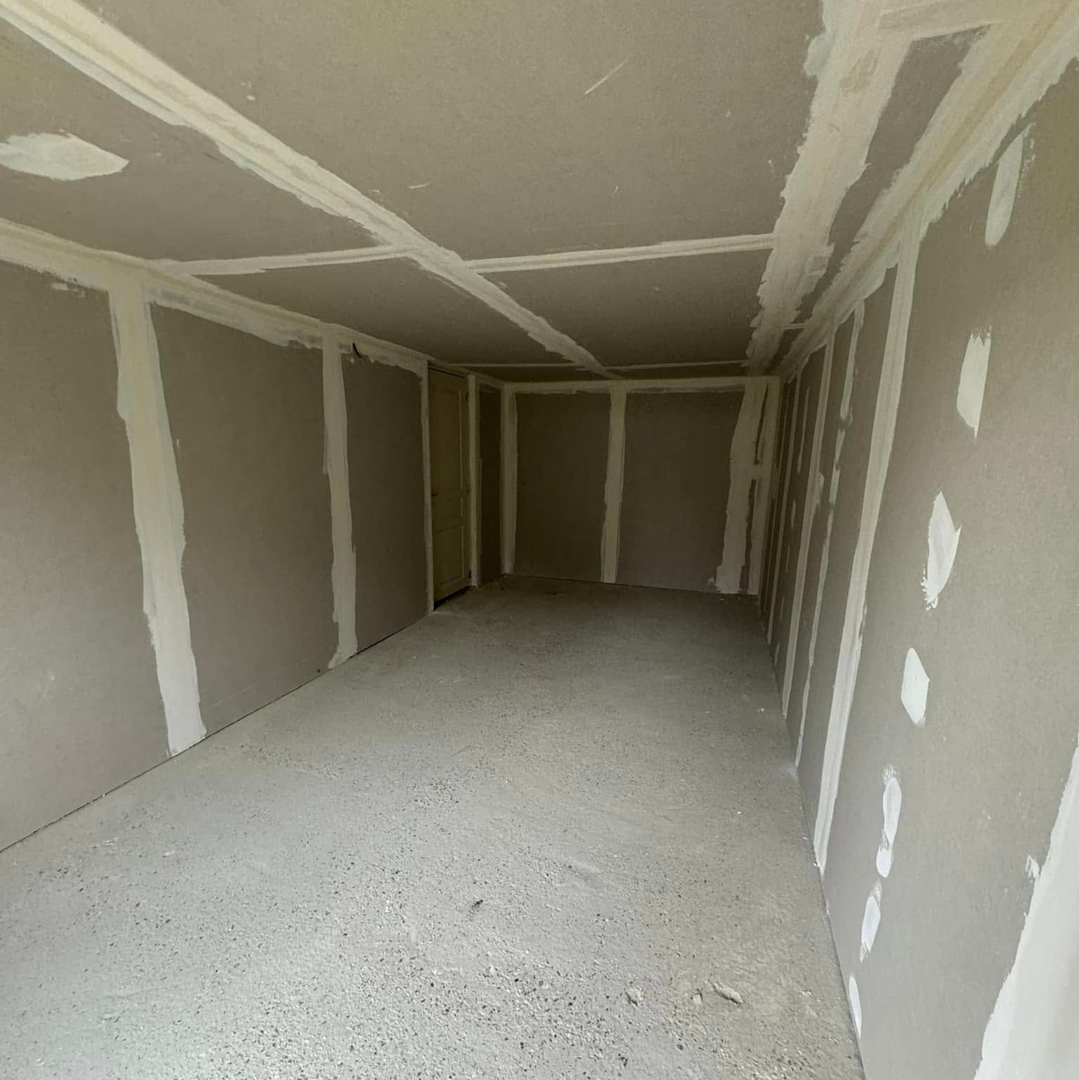 Intérieur d'une pièce avec des murs et un plafond en plaques de plâtre non finies, des joints collés et un sol en béton.