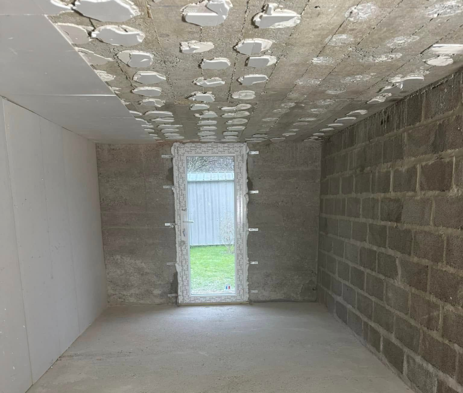 Intérieur d'une pièce en construction avec des murs en briques apparentes, un sol en béton.