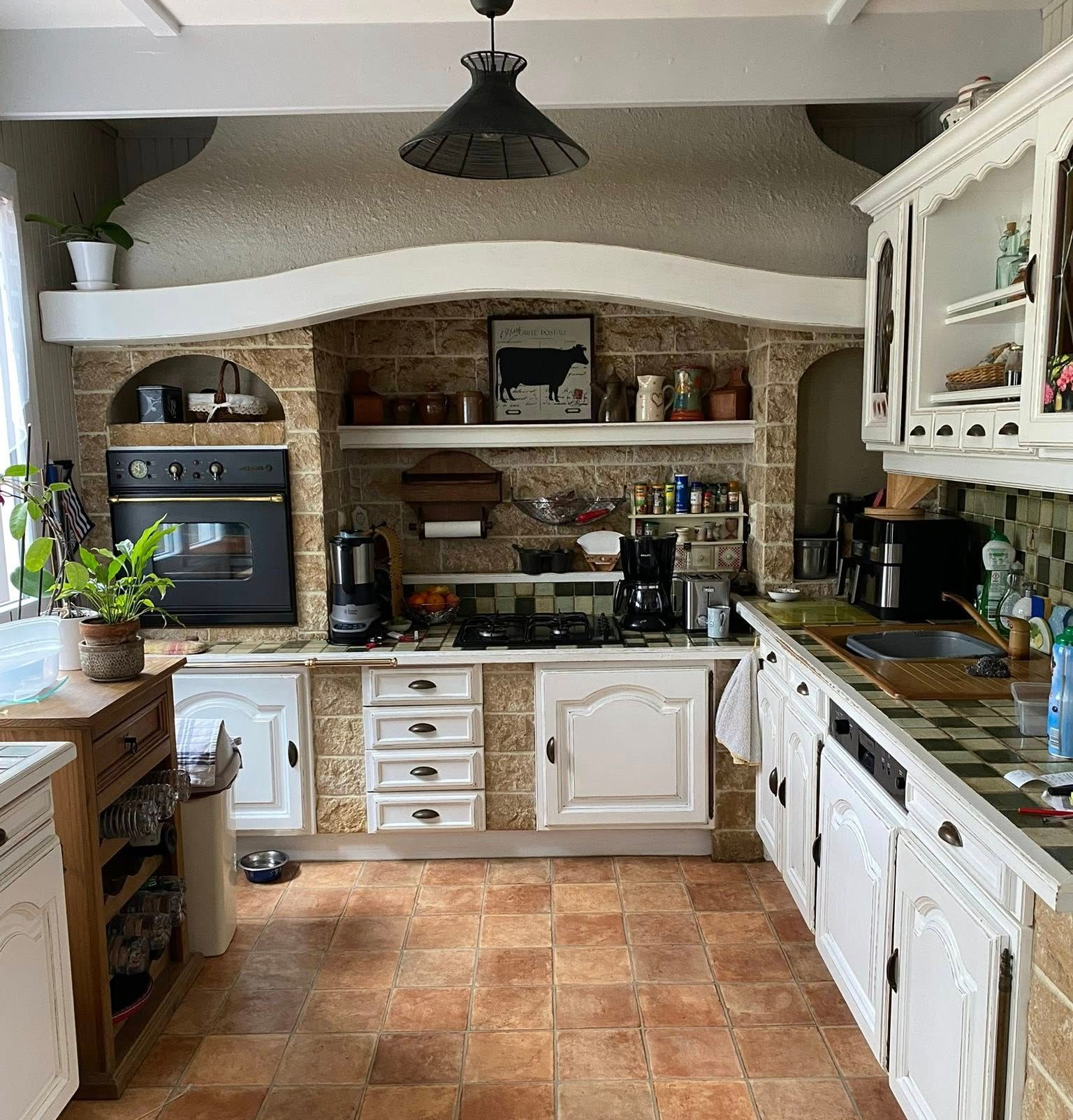 Cuisine avec placards blancs, crédence carrelée, four encastré et sol en terre cuite.