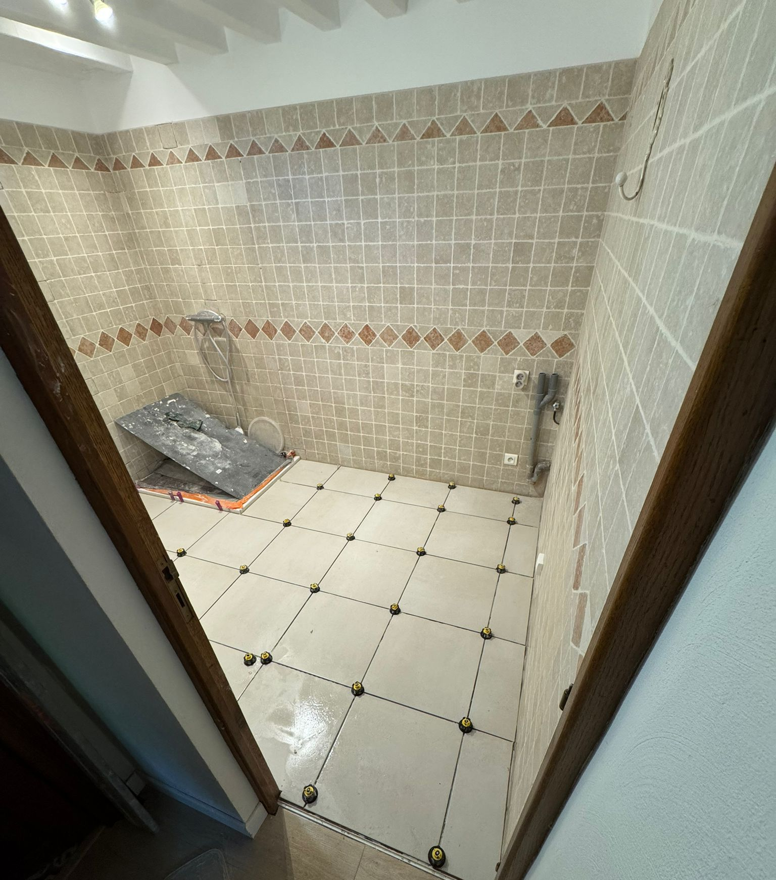 Pièce vide aux murs beiges, aux moulures blanches et au parquet foncé. Une porte ouverte donne sur un couloir sombre.