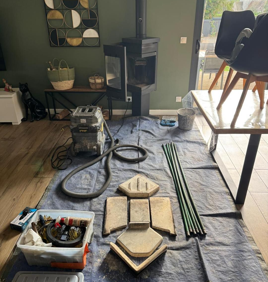 Poêle à bois démonté pour être nettoyé, le matériel étant étalé sur une bâche à l'intérieur d'une maison.