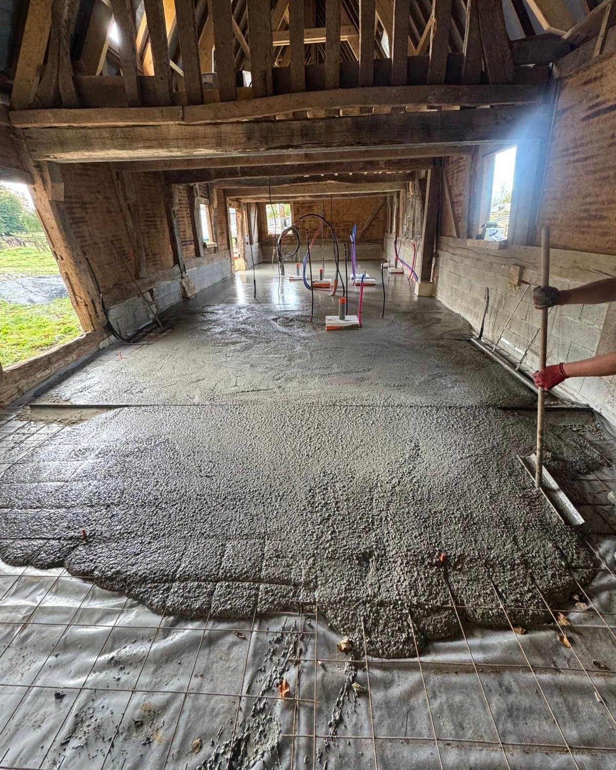 Du béton est coulé dans une longue structure à ossature bois, avec des outils et une personne visibles.