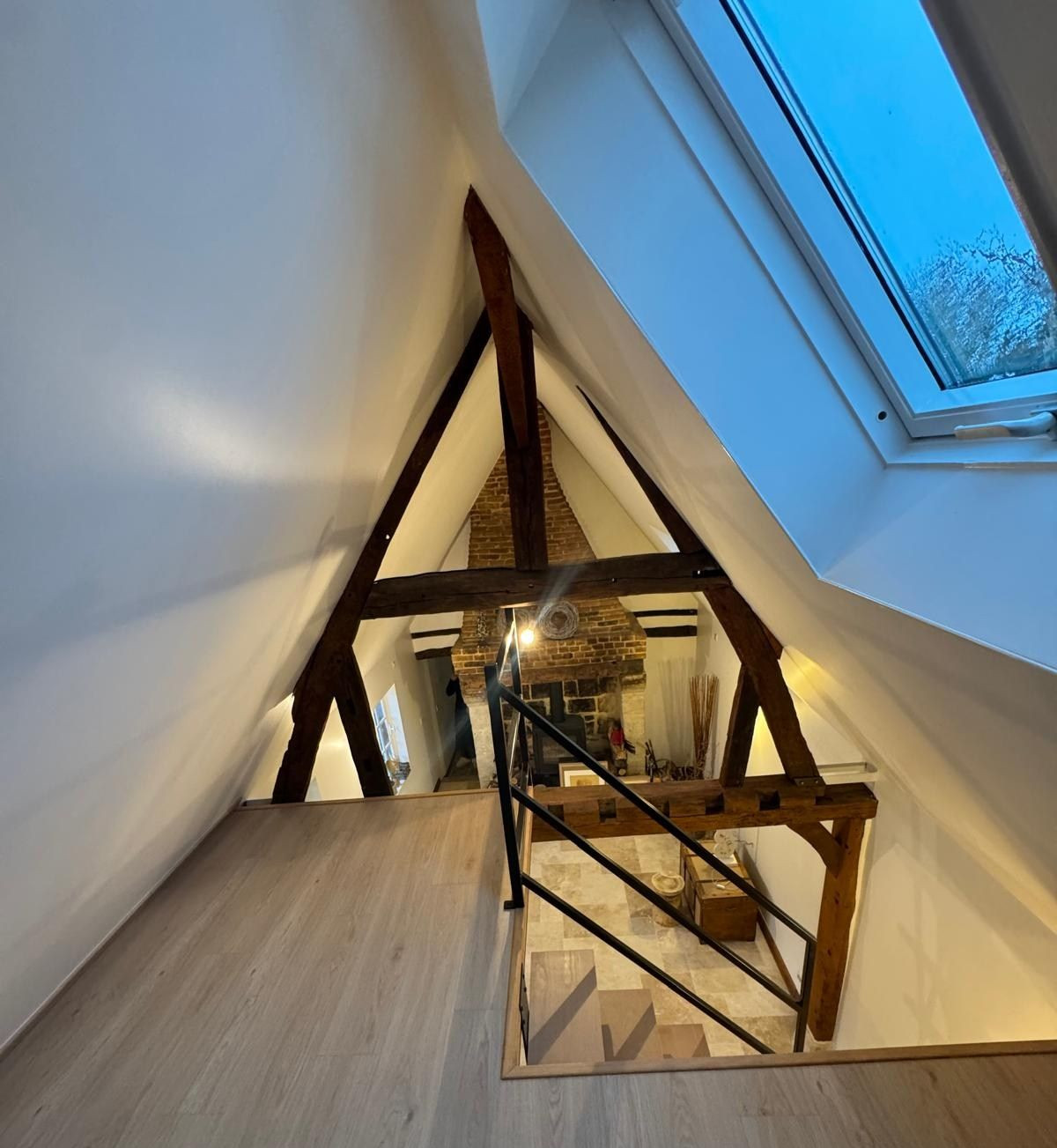 Pièce mansardée avec murs blancs en pente, poutres apparentes, escalier et puits de lumière.