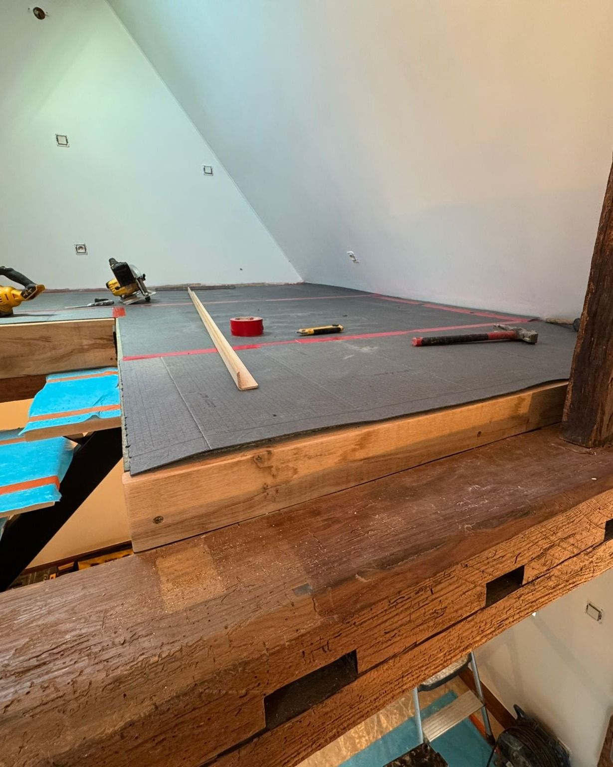 Poutres en bois soutenant un grenier en construction, avec isolation et niveau déjà en place.