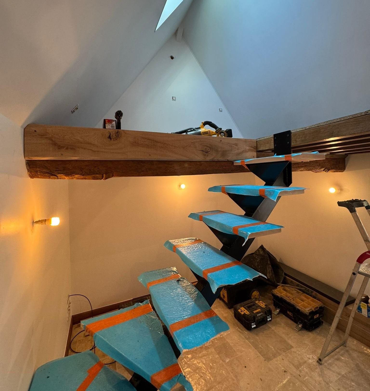 Un escalier moderne est en construction dans une pièce lumineuse au plafond mansardé.