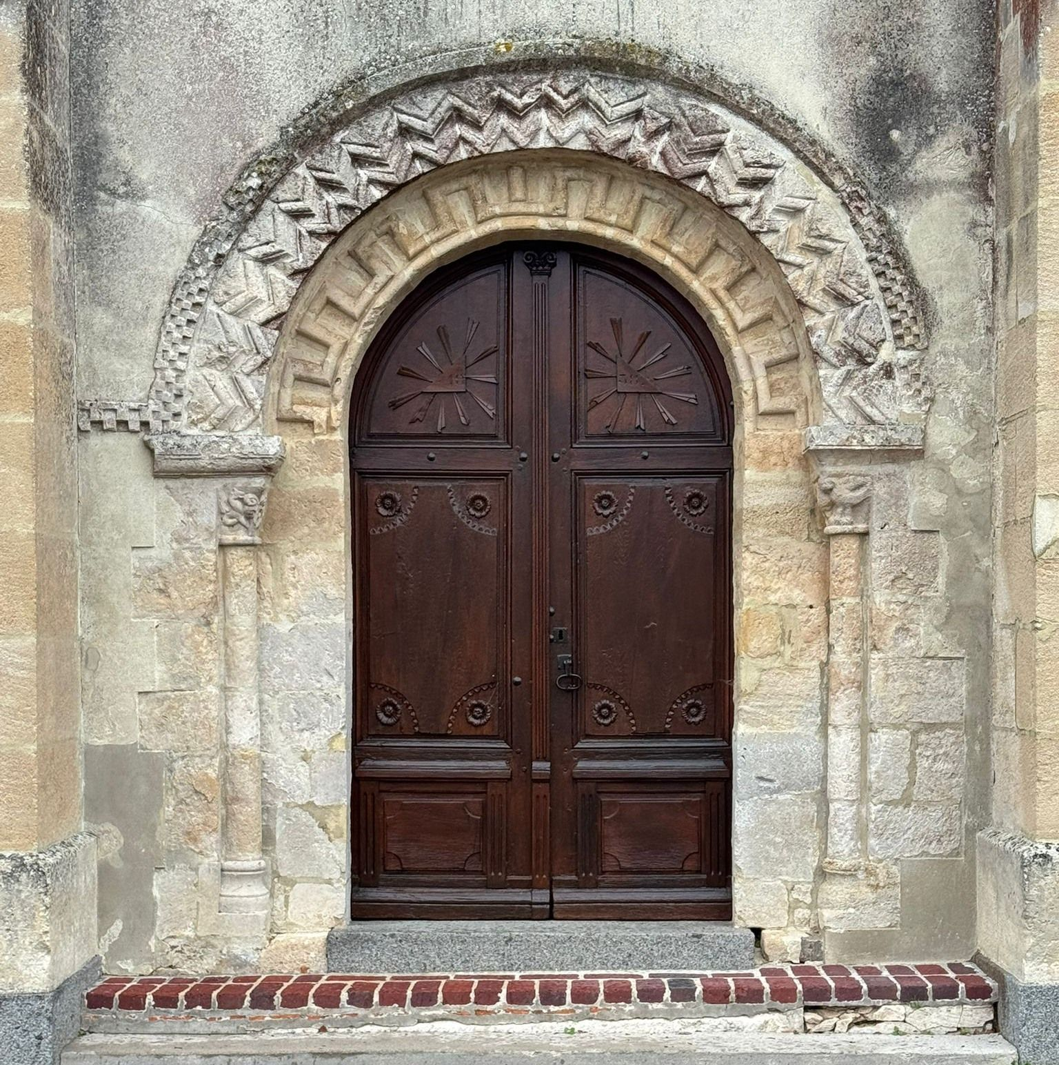 Porte cintrée en bois dans un bâtiment en pierre avec arche sculptée décorative.