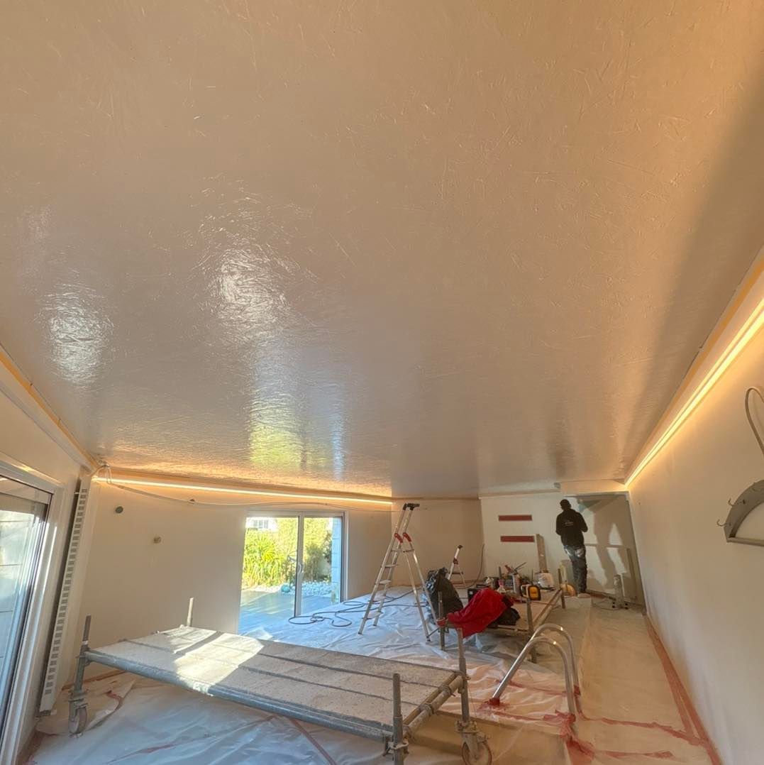 Pièce en rénovation, plafond blanc immaculé, éclairage encastré, sol recouvert.