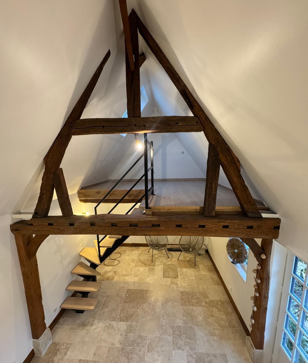 Vue intérieure d'un loft avec poutres en bois, escalier et plateforme au deuxième étage.