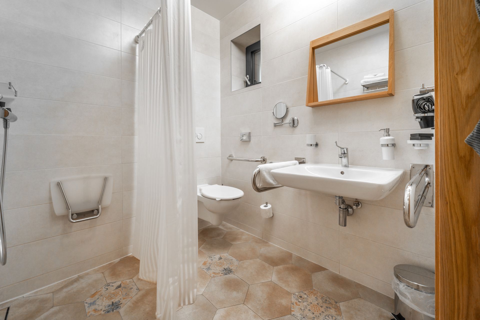 Salle de bains accessible avec douche, toilettes et lavabo ; murs blancs, sol neutre et barres d'appui.